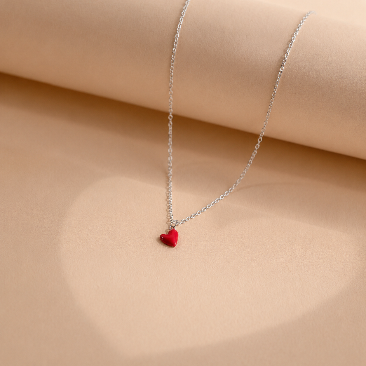 Silver necklace with a red heart pendant on a beige fabric background